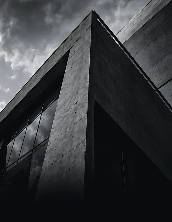 Platinum-toned low-angle view of a dark concrete and glass building corner against a stormy sky